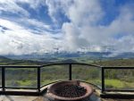 OVID Winery's outdoor terrace with a stone fire pit in the foreground overlooking a dramatic cloud-filled Napa Valley from Pritchard Hill