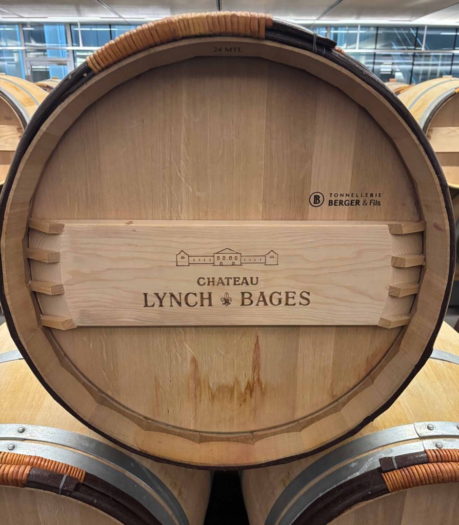 Overhead close-up of a new oak barrel head stamped with the Château Lynch-Bages name and cooperage marking in the barrel room