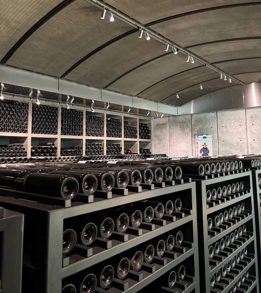 Dramatic underground cellar at Lynch-Bages with sweeping curved concrete walls and illuminated bottle storage receding into the distance