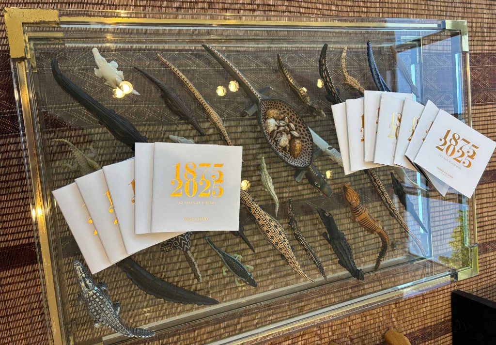 Glass display table at Château Lynch-Bages filled with decorative alligator sculptures and 1875–2023 anniversary booklets