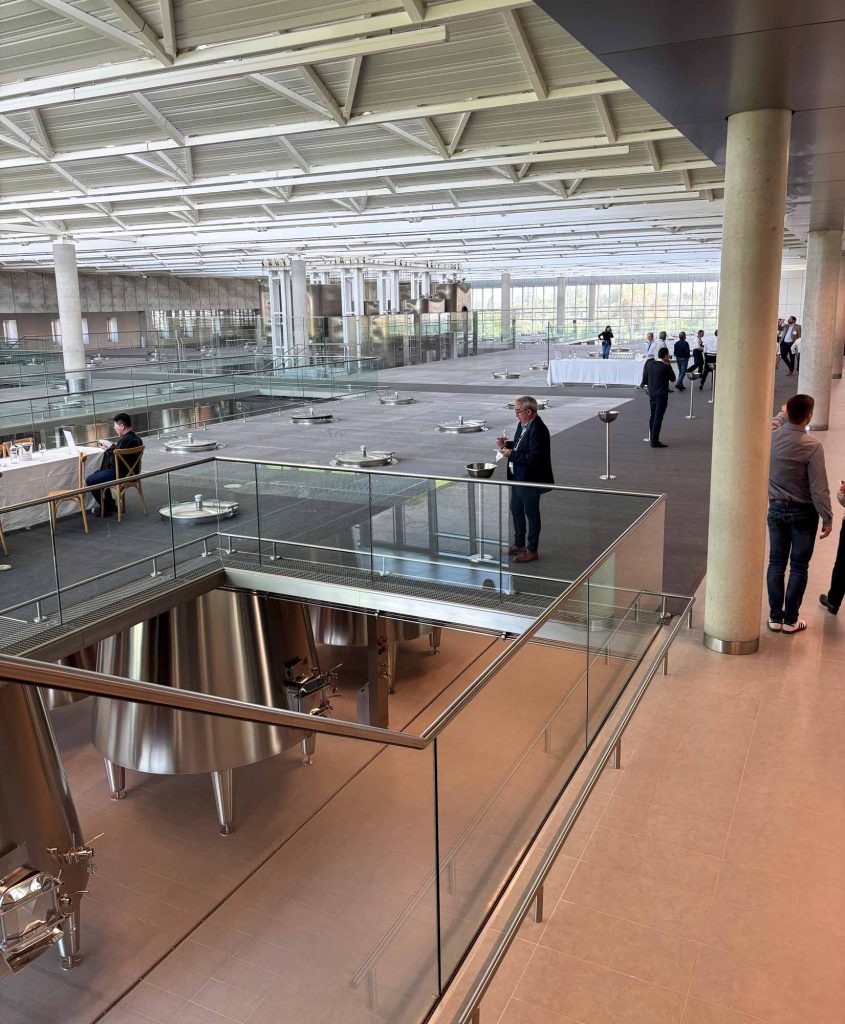 Wide view of the new Lynch-Bages winemaking facility showing elevated glass walkways over rows of stainless steel fermentation tanks
