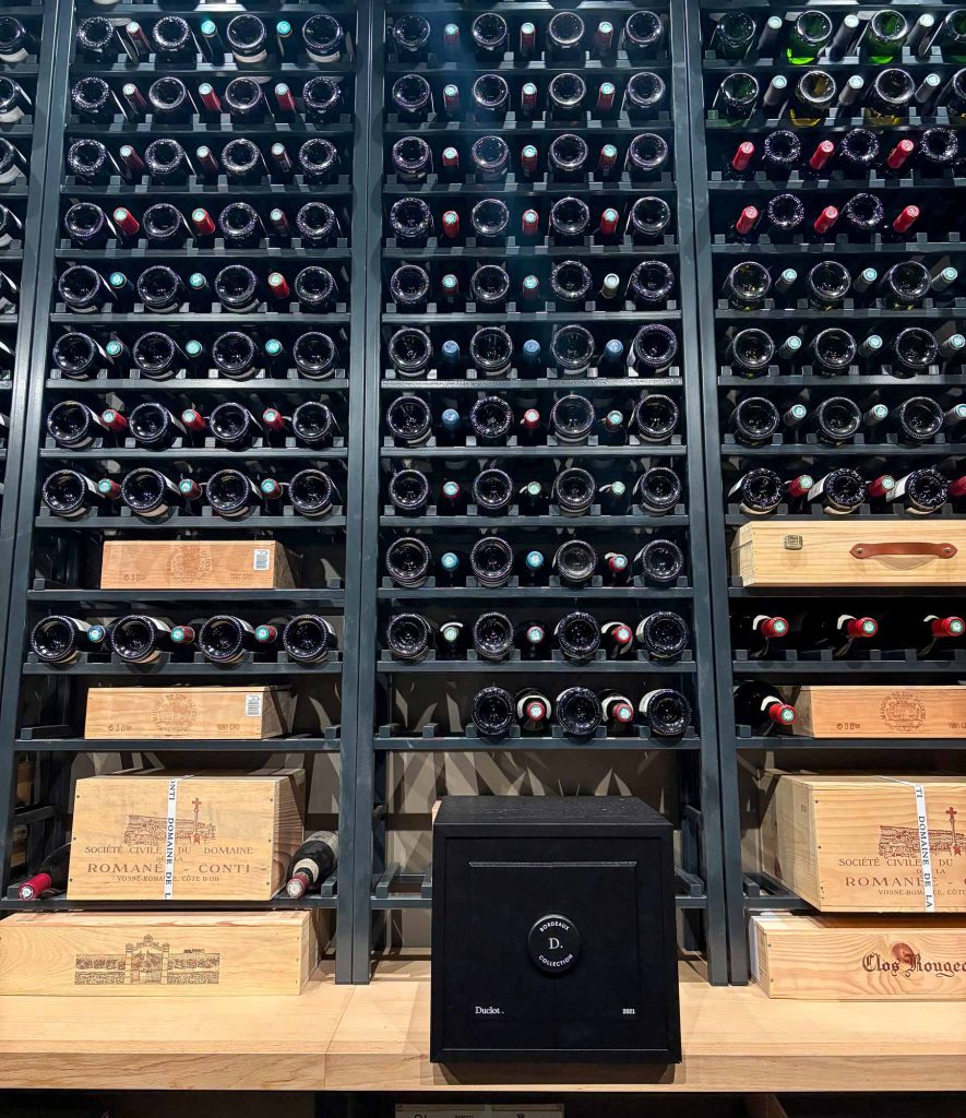 Floor-to-ceiling wine racks packed with bottles in the Lynch-Bages private cellar, with wooden cases of fine Burgundy visible alongside