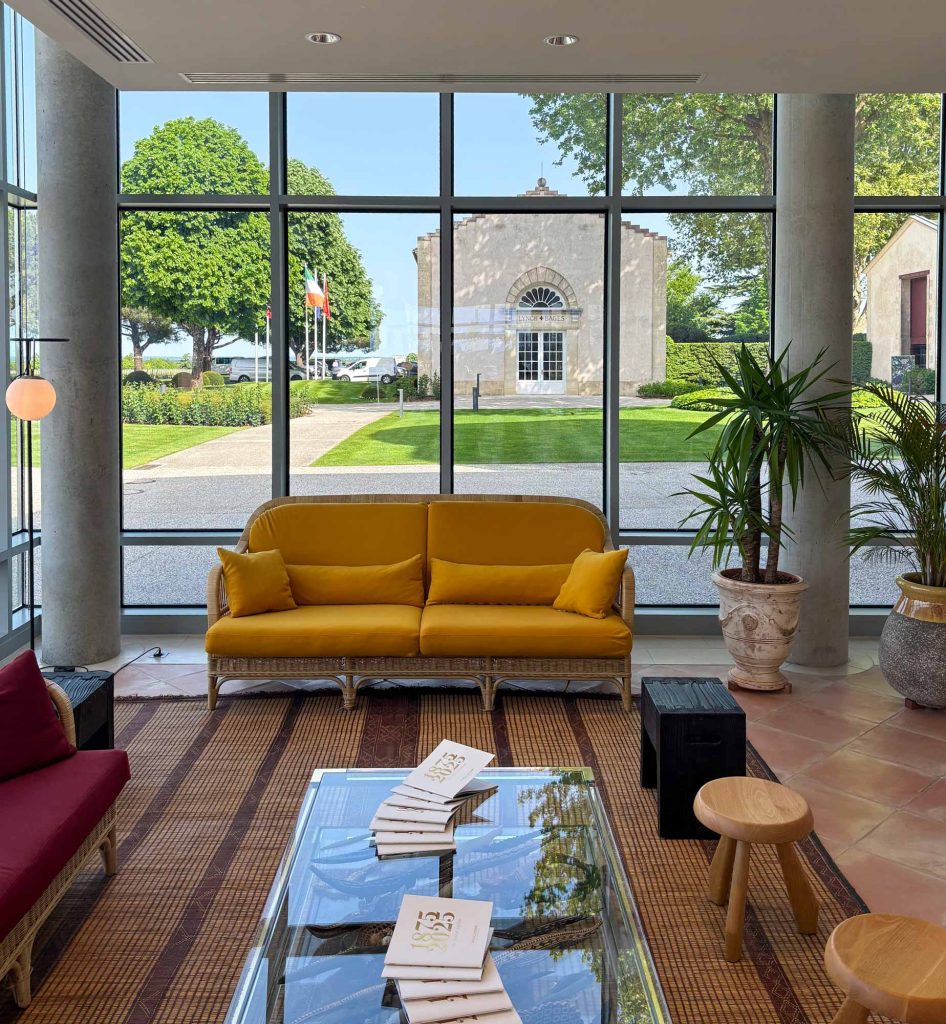 Modern reception interior at Château Lynch-Bages with yellow sofa and floor-to-ceiling windows overlooking the historic château building